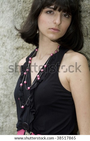 An 18 year old exotic brazilian model, with short dark hair, a young looking face and a skinny body. She is wearing a black dress and pink belt.