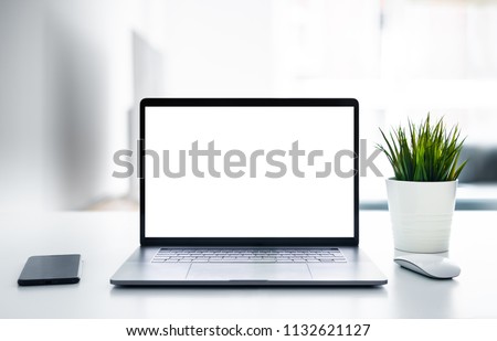 Laptop with blank screen on white table with mouse and smartphone. Home interior or office background