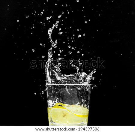 Lemon splashing water in glass - isolated on black