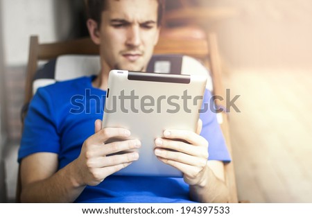Man lying on a lounger and using tablet device.