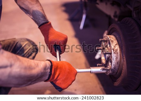 Male mechanic hands in gloves tightening the nuts using wrench. Mending, repair car in workshop.