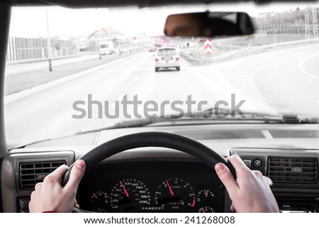 Driving a car. Hand on steering wheel of a car driving on a road. Focus on clocks.