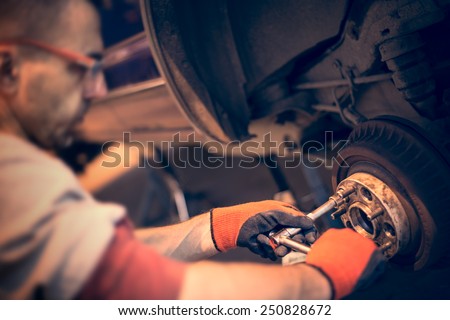 Male mechanic in gloves tightening the nuts using wrench. Mending, repair car in workshop.