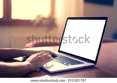 Man\'s hands using laptop with blank screen on desk in home interior.