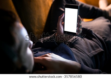 Man relaxing during listening to the music while lying on sofa - blank screen smartphone