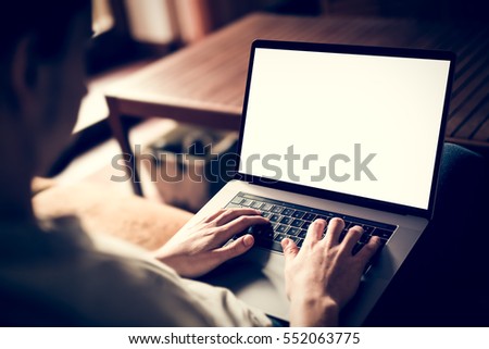 Man using, working on laptop with blank screen while sitting on sofa in living room. mockup template
