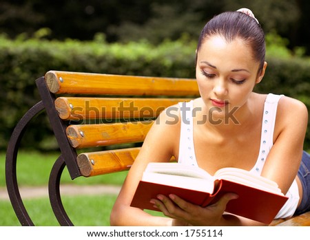 The young girl reads the book in park on a bench