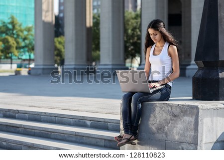 A young woman with a laptop sitting on the stairs, near the university
