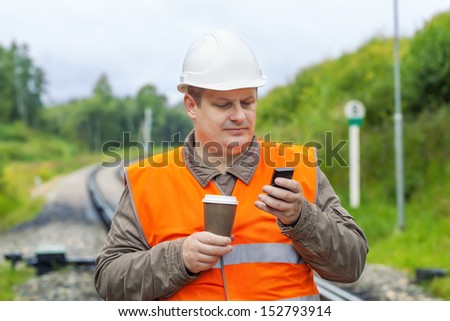 Worker with cell phone and coffee on the railway