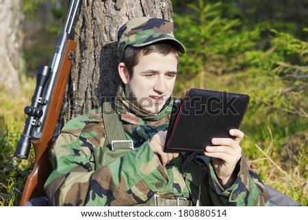 Young recruit with tablet PC and optical rifle in forest