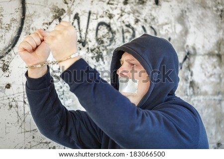 Hostage in handcuffs with tape on the mouth near wall