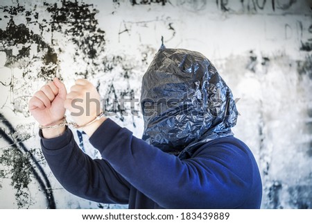 Hostage in handcuffs and with a bag on head near wall