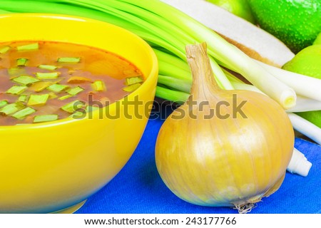 Onion near bowl of onion soup and with spring onions in background