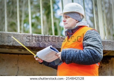 Engineer with tape measure and documentation under the bridge
