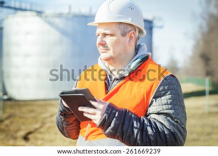 Engineer working with tablet PC near oil tank
