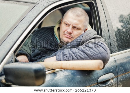 Aggressive man with a baseball bat in car at outdoors