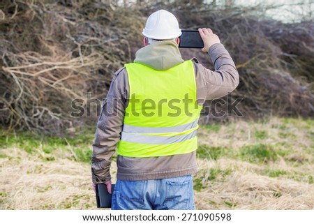 Forest engineer with tablet PC near pile of twigs