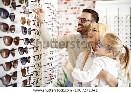 Four year little girl in optics store choosing glasses with her father. Ophtamologist helping.