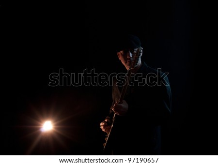 man wearing a black hat , playing guitar on a black background,