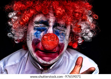 close up of a sad , upset , crying clown with a red nose on a black background