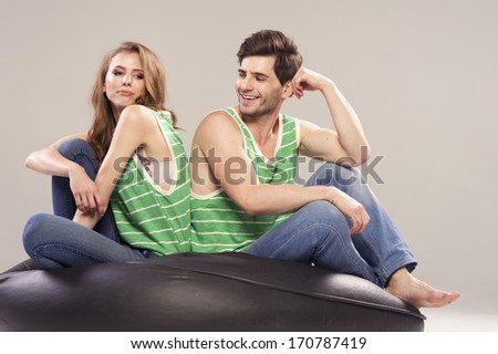 Cheerful young couple sitting with back to each other on floor, he cheerful and she offended
