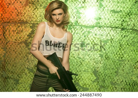 portrait of sexy blonde  with gun against camouflage net