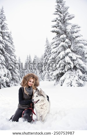 Happy young woman playing with siberian husky dogs in winter forest
