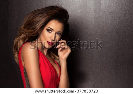 Sensual beautiful brunette woman posing in red dress. Girl with long curly hair.