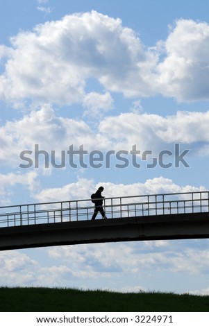 Young man crossing bridge against bright blue sky
