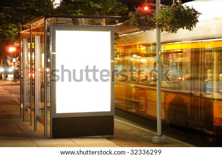 Bus stop billboard at night. Bus passing by