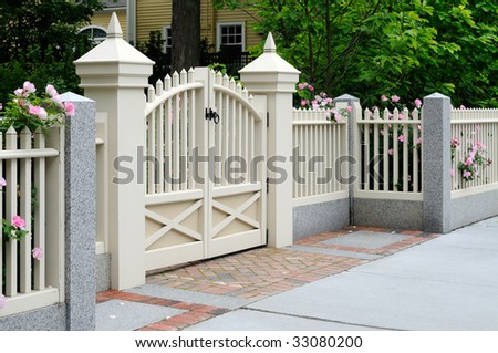White gate and fence with pink roses on house entrance. Elegance, craftsmanship, home improvement.
