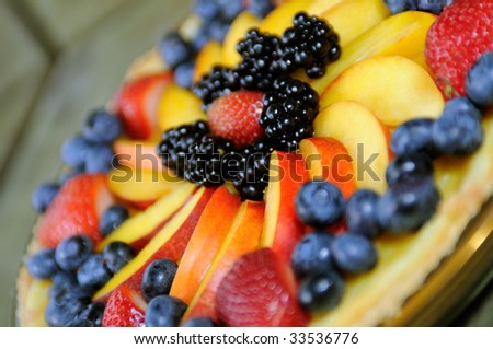 Fruit tart or custard pie with colorful berry mix. Strawberry, blueberry, blackberry and peach. Close-up, tilt, selective focus.