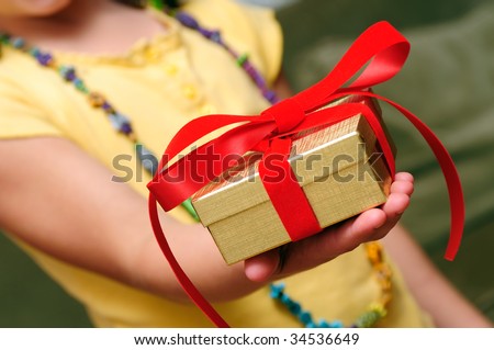 Child giving gift with red bow and golden box. Hand close-up.