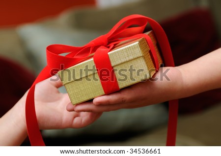 Child giving gift with red bow and golden box. Hand close-up.