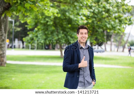 Young Casual Man Showing Thumbs Up And Smiling In The Park.