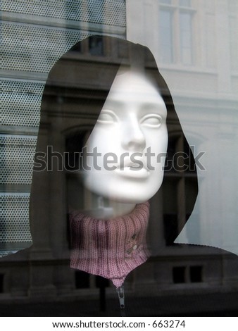 Plastic mannequin behind shop window with reflection