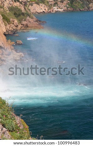 Limpid waters of the Duden Falls (Antalya,Turkey)  drop off a rocky cliff directly into the Mediterranean Sea in a dazzling show. A rainbow is against the blue sea.