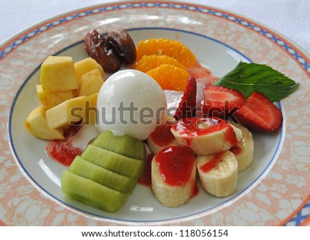 Fruit dessert contains from ice-cream, banana, dates, kiwi, orange, strawberry. Dessert is decorated with mint leaves and strawberry jam.