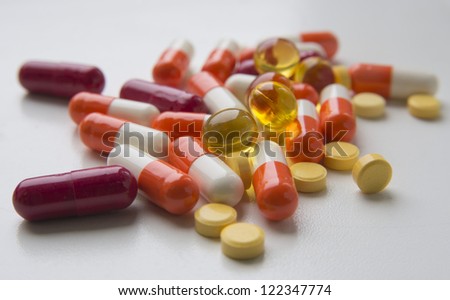 Pharmaceutical products are spilled on the table. Varied in colour medicaments are situated against the white background.