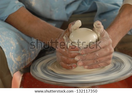 This is pottery making. A craftsman\'s hands shape clay into a vase on a spinning wheel.