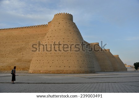 Fortress Ark (Uzbekistan) is situated against the blue sky background. Little figure of a tourist (woman) emphasizes strength of the fort.