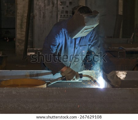 Working man with helmet shield on his head is welding  steel construction. Hard work in the production department.