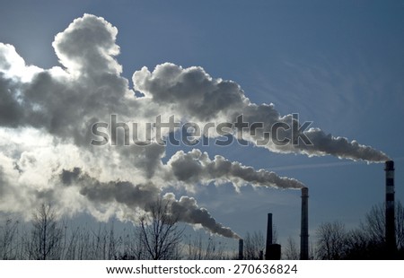 Factory tubes and white smoke against blue sky. Industrial scene.