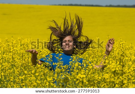Girl dressed in blue is jumping on yellow field. Girl\'s dark hear is flying. Story about positive emotions.
