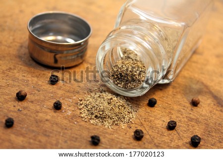 Pepper shaker with unscrewed cap with pepper spilled on table