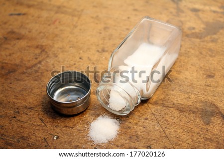 Salt shaker with unscrewed cap with salt spilled on table