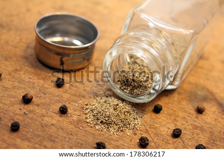 Pepper shaker with unscrewed cap with pepper spilled on table