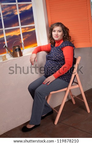 Young pregnant woman sitting on the chair at sunset in the city
