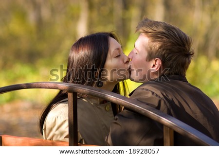 Young couple kiss on a bench in autumn park