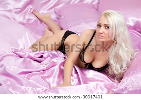 Young caucasian woman lies in bed on pink silk sheets